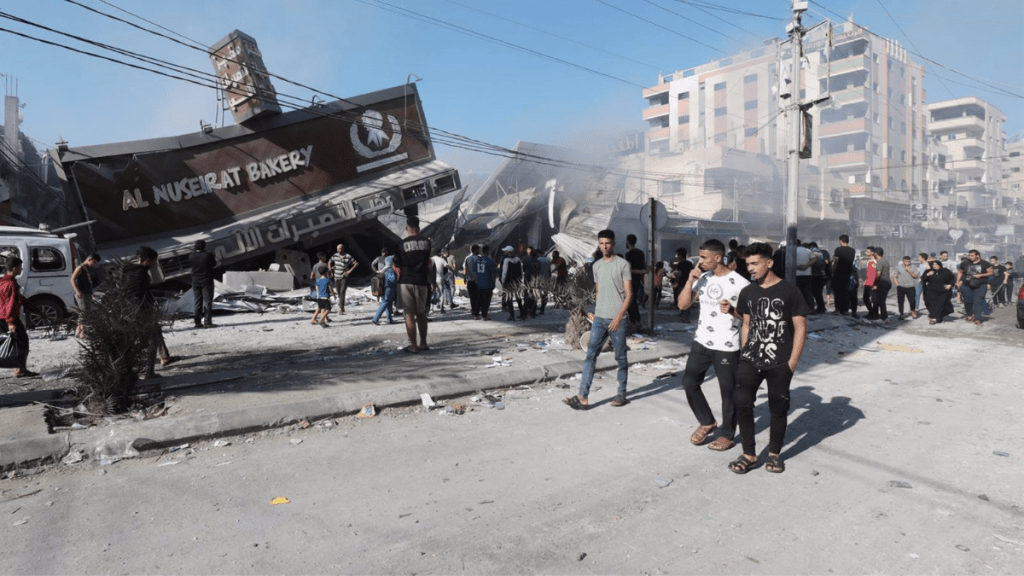 Un grupo de palestinos frente a una panadería destruida por un bombardeo de Israel