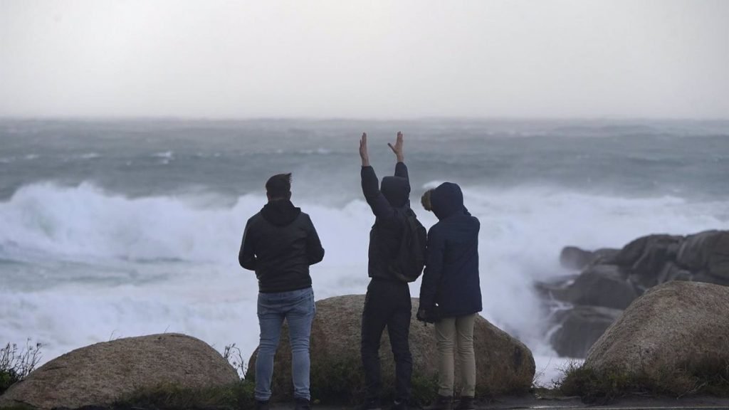 Tres jóvenes miran y fotografían el mar embravecido