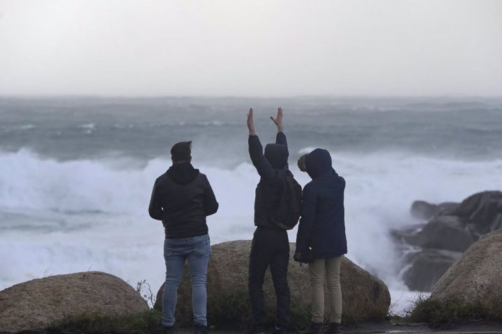 Tres jóvenes miran y fotografían el mar embravecido