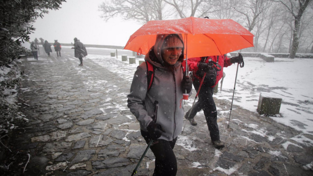 Una nieve y vientos persona camina con bastones y ropa de abrigo mientras nieva en la parroquia de O Cebreiro | EP