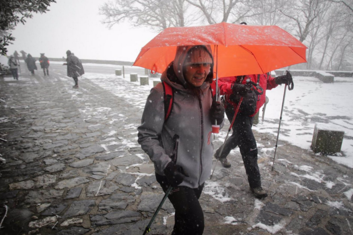 Una nieve y vientos persona camina con bastones y ropa de abrigo mientras nieva en la parroquia de O Cebreiro | EP