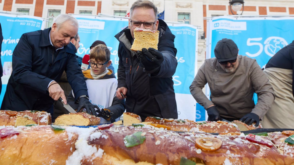 Varias personas cortan el roscón de reyes de Aldeas Infantiles