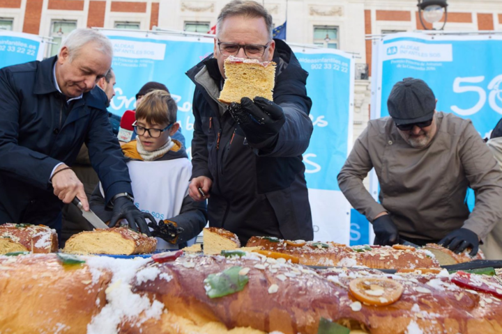 Varias personas cortan el roscón de reyes de Aldeas Infantiles